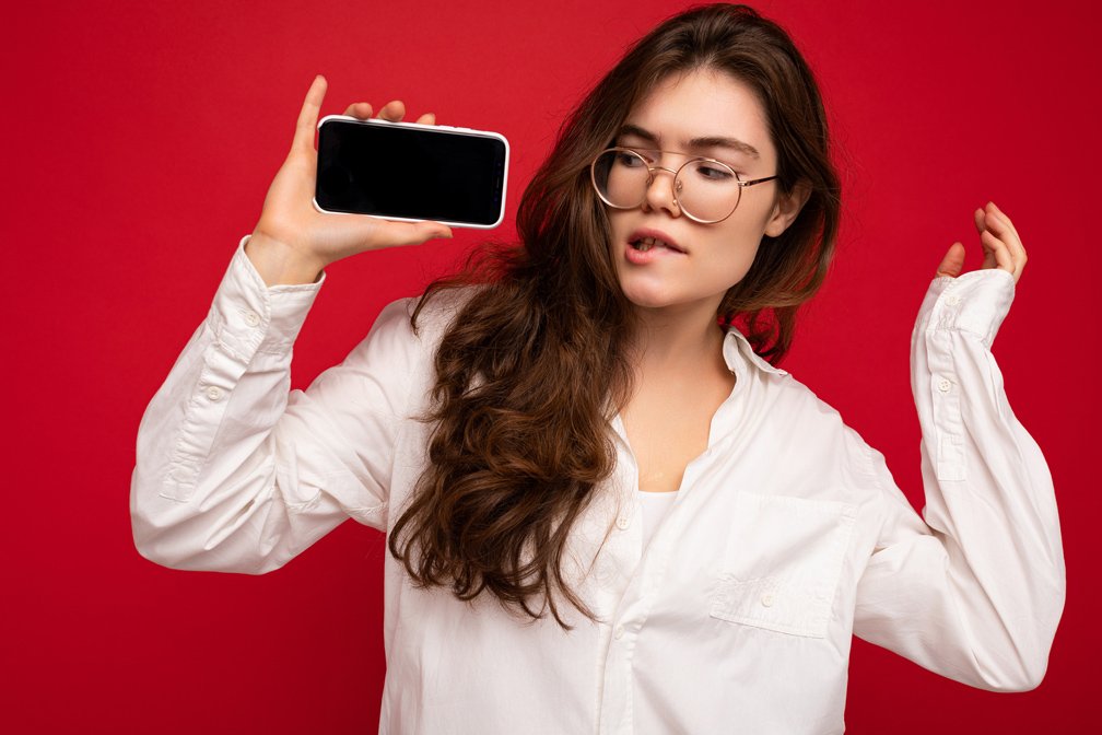 Chica joven, sosteniendo un smartphone sobre fondo rojo.